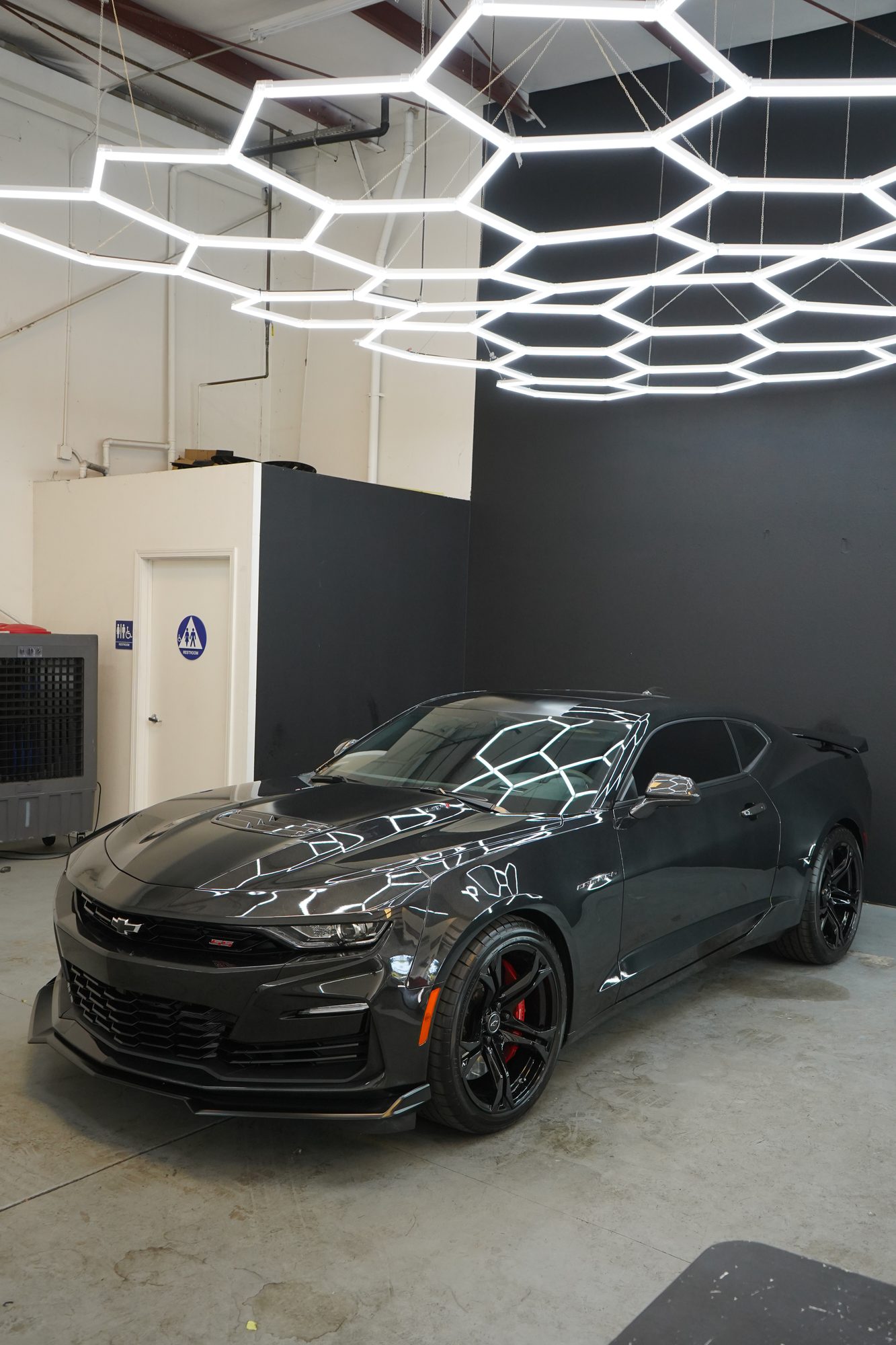Dark grey Chevrolet Camaro parked under the hex lights inside the Oakdale shop after a ceramic coating