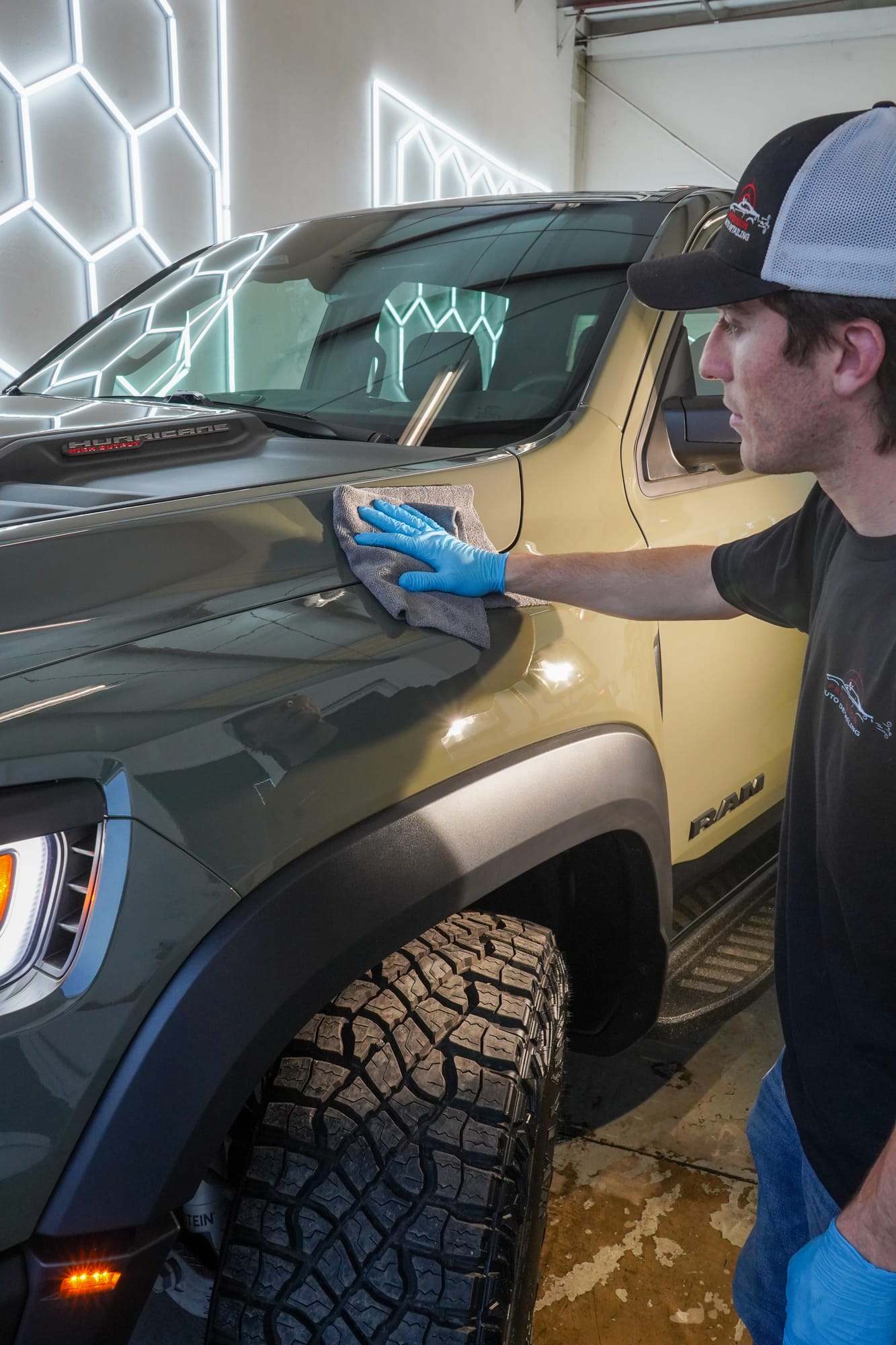 A detailer in blue gloves working a ceramic coating across the hood of a Ram RHO