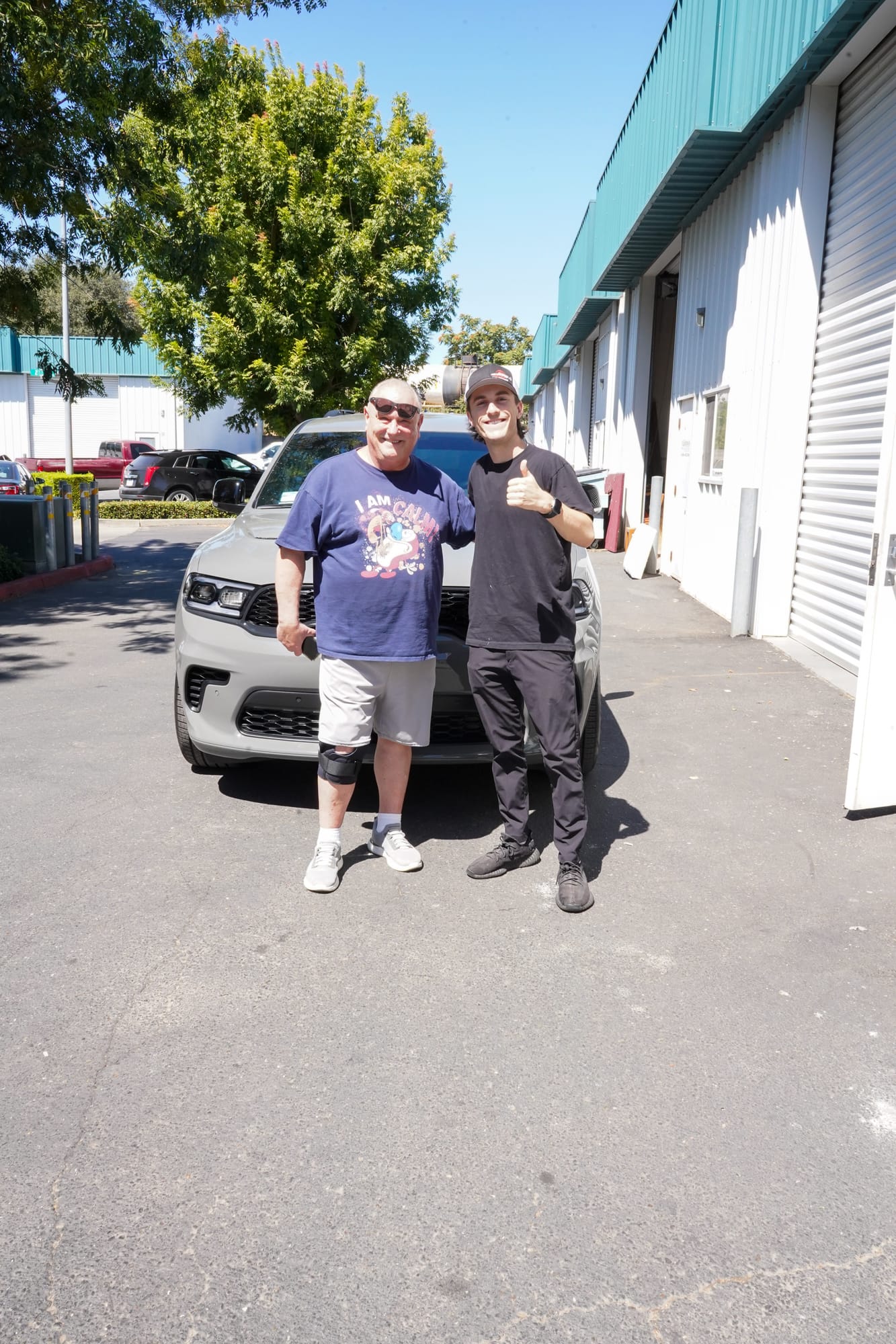 A customer and a Precision Auto Detailing team member beside a grey Dodge Durango with new paint protection film, outside the Oakdale shop