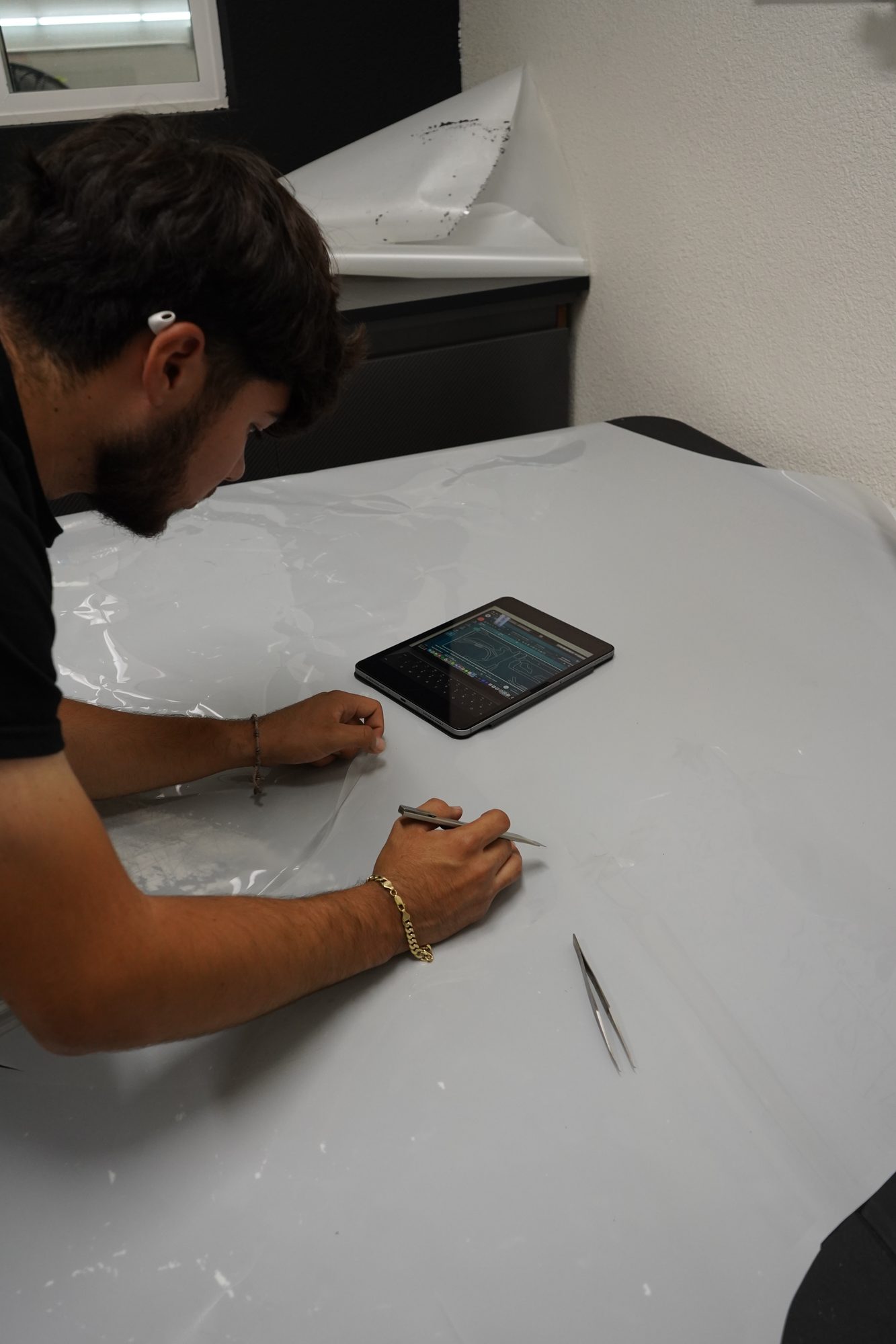 An installer laying paint protection film across a hood, the cut pattern on a tablet beside him