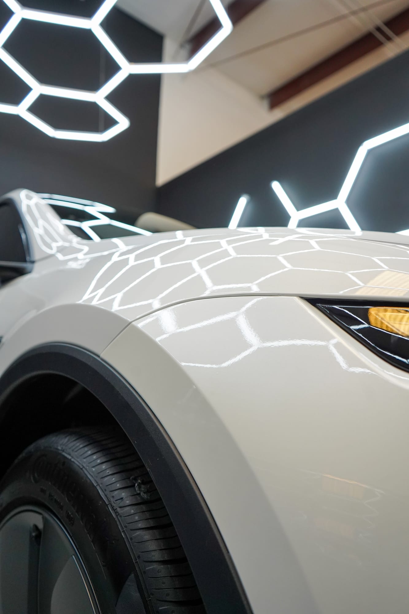 Close up of paint protection film on a Tesla's front fender and bumper, hex lights reflected