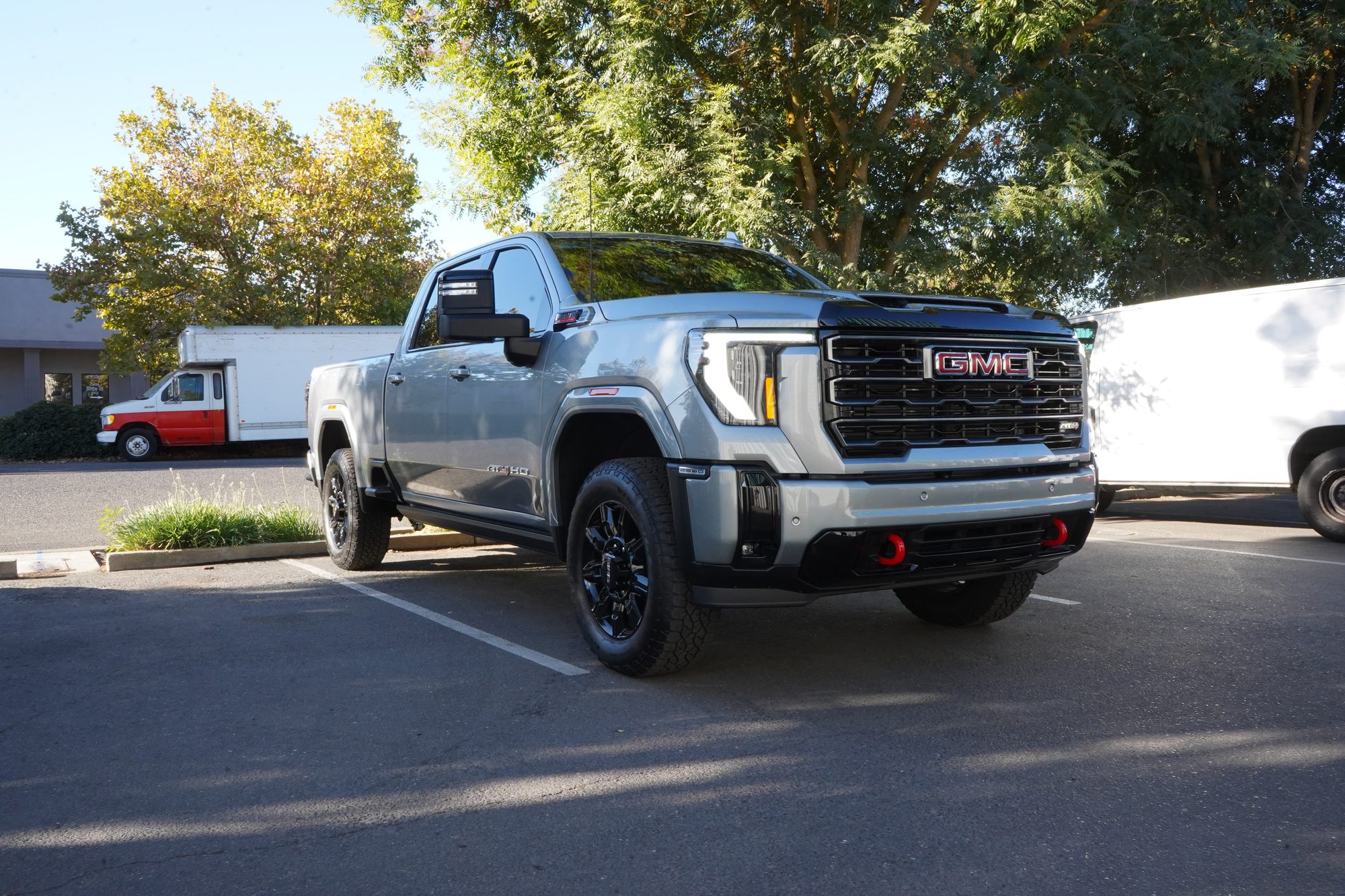 Silver GMC Sierra AT4 HD with tinted windows, parked outside the shop under the trees